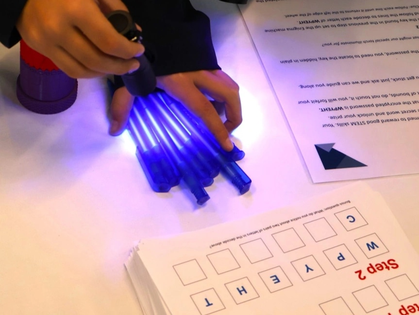 Students inspect pens under a black light whilst trying to solve a cypher
