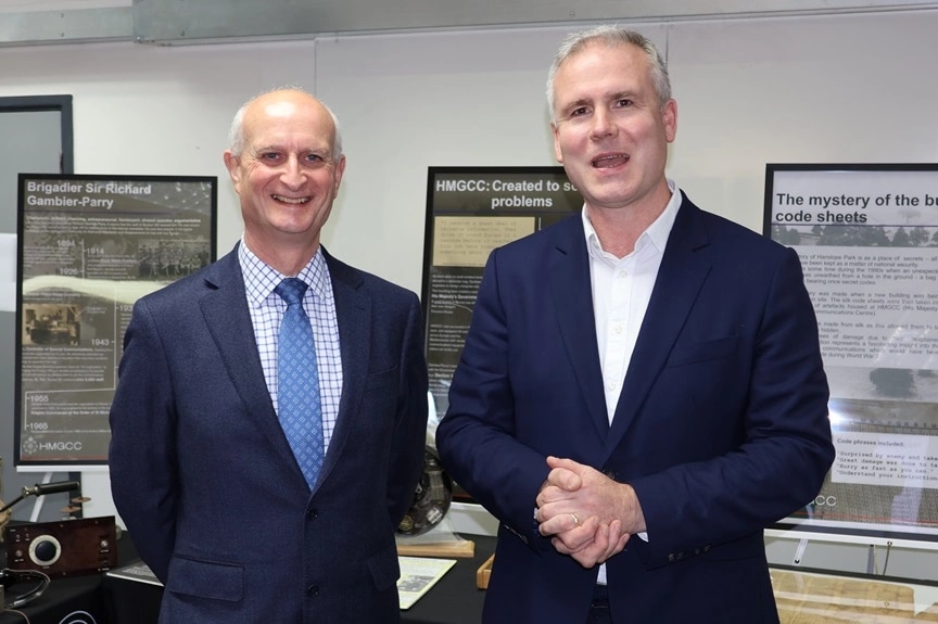 HMGCC CEO George Williamson and Bletchley Park CEO Iain Standen stand in front of historic artefacts.