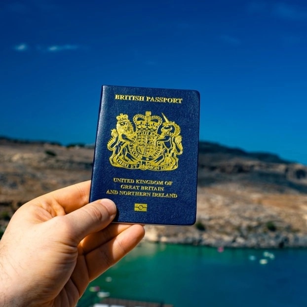 image shows a hand holding a passport with a coastal image behind