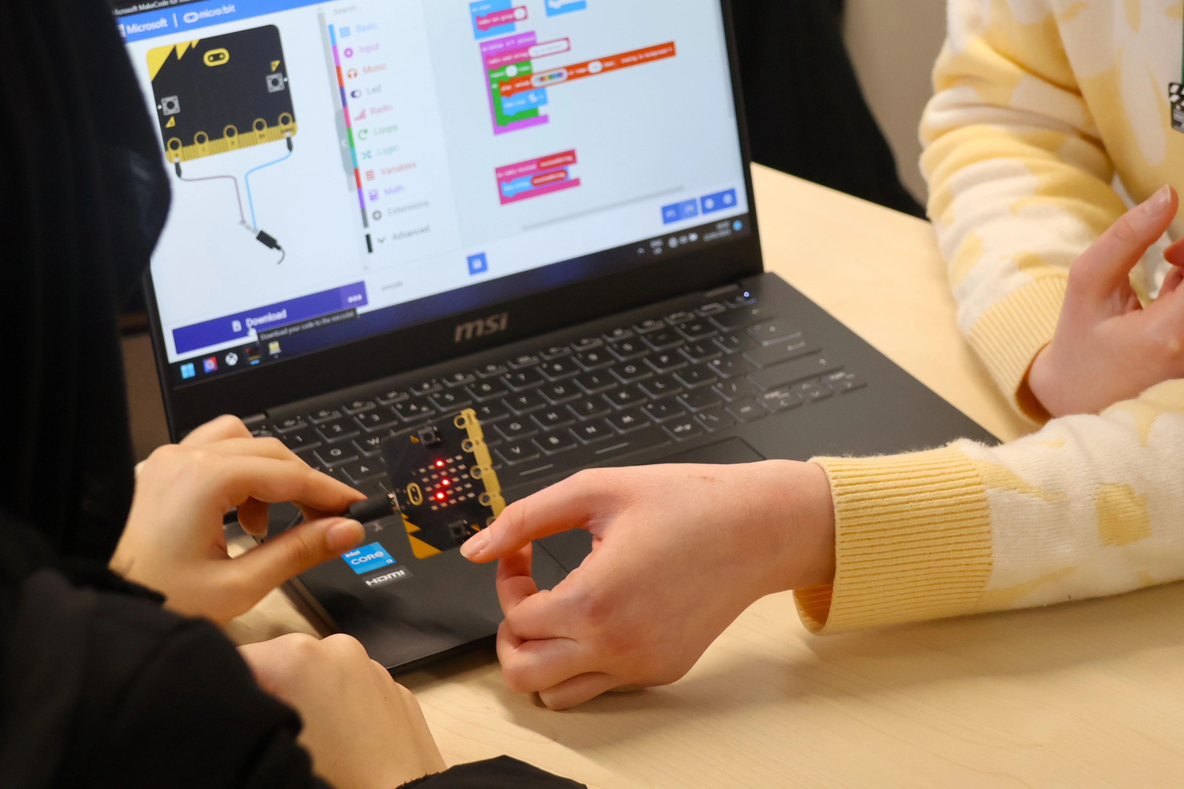 Image shows the hands of two school children holding a microbit as they work on a STEM challenge